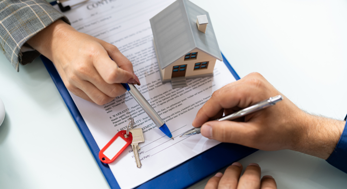 Signing a real estate contract with a miniature house model on the document.