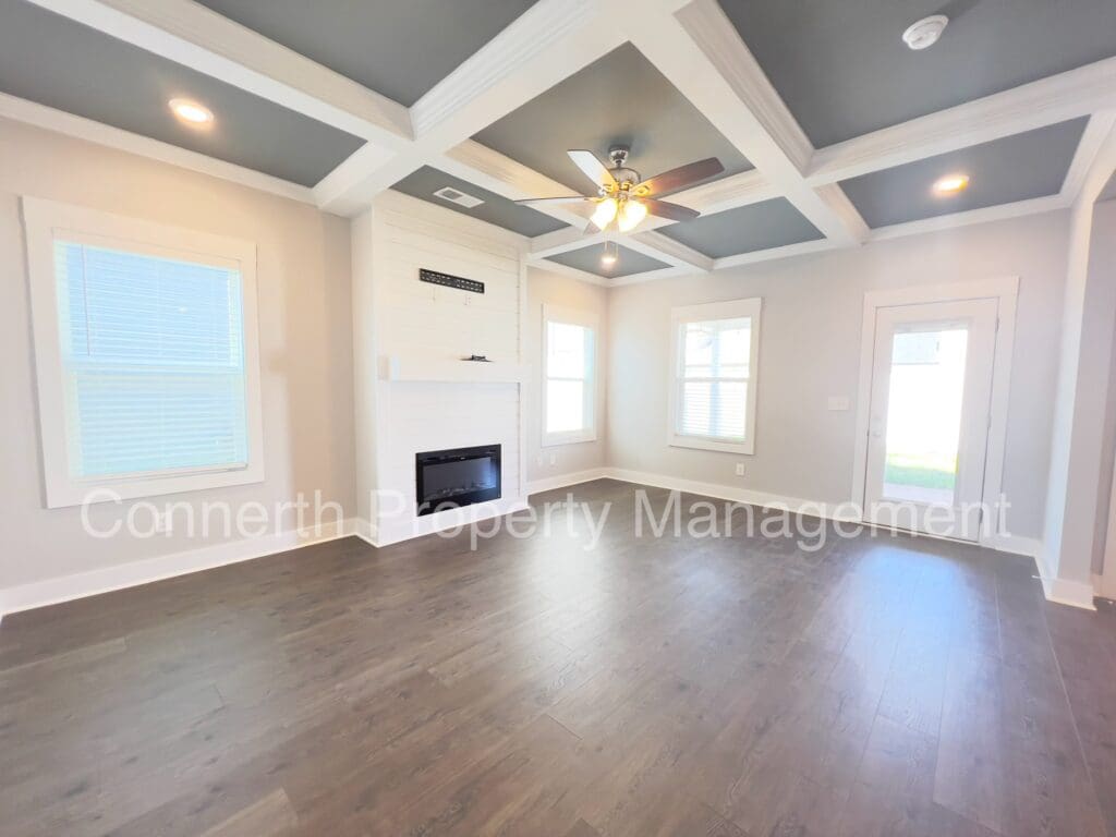 Empty living room with coffered ceiling, hardwood floors, and a ceiling fan