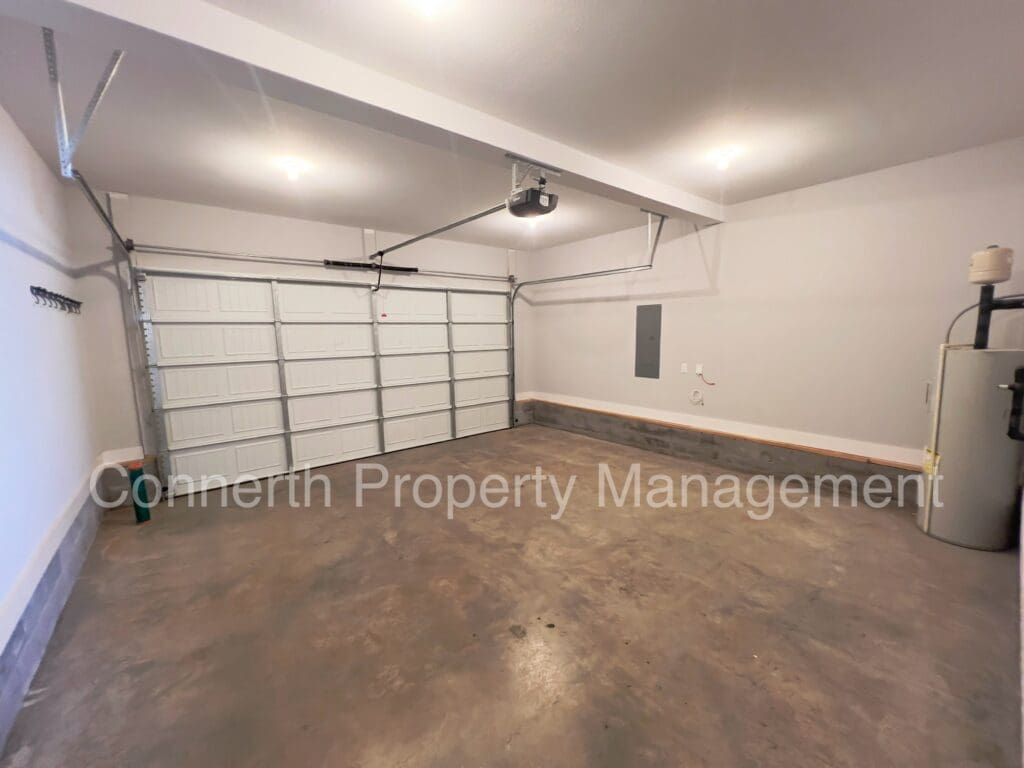 Interior of a clean, empty garage with a white door, concrete floor, and overhead lighting. a water heater is visible in the corner. text overlay: cornerth property management.