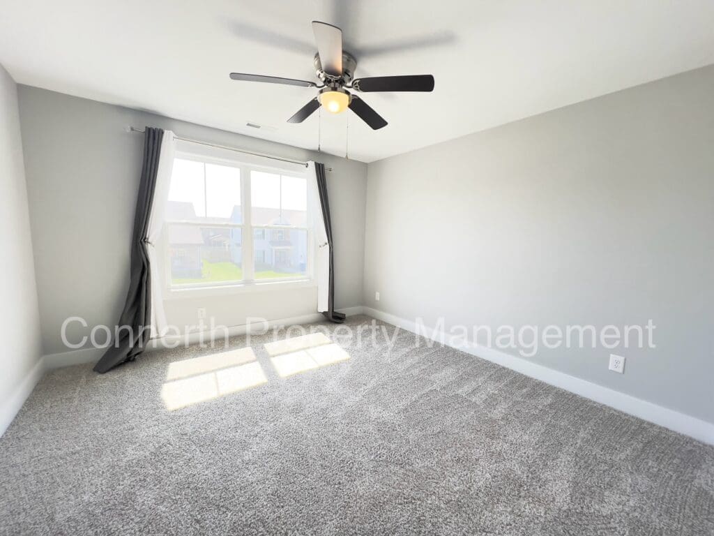 Empty room with gray carpet, bay window with curtains, ceiling fan with light, and walls with watermark 