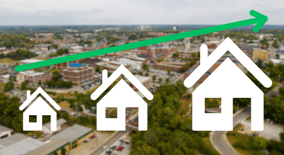 A green upward arrow crosses over an image of a city, with three white house icons increasing in size from left to right, representing rising housing market trends.