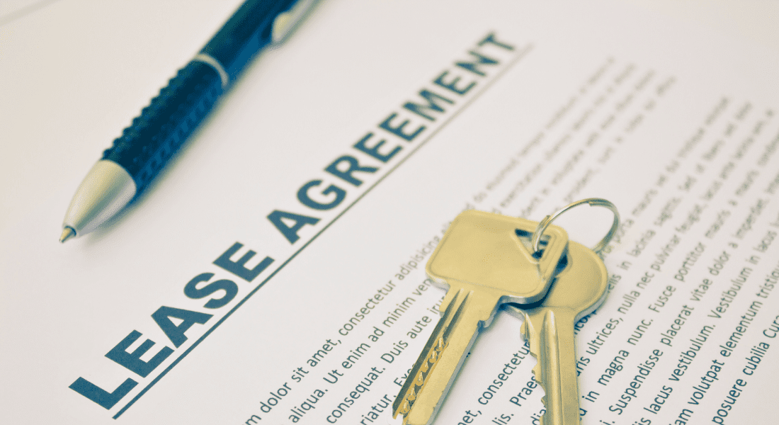 A lease agreement document is laying on a table with a pair of keys and a pen on top.