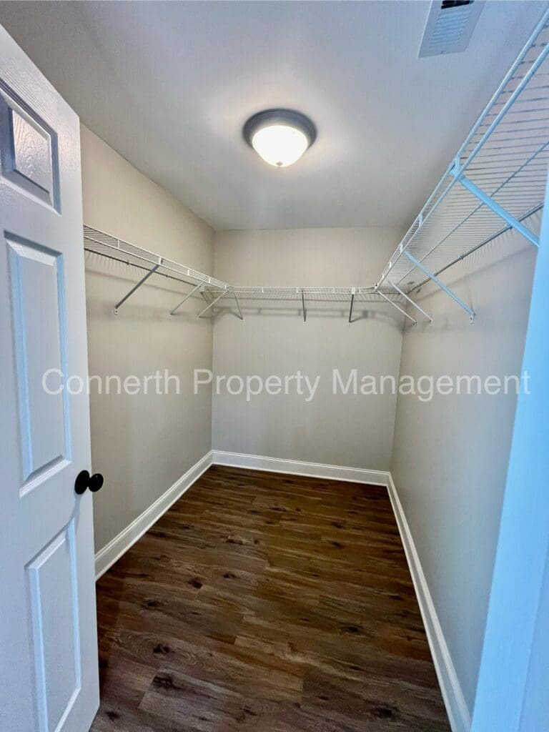 Empty walk-in closet with white wire shelves, wooden flooring, and a closed white door.