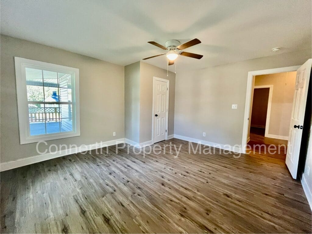 Empty room with wood flooring, light gray walls, a ceiling fan, and a window on the left. A closet door and open doorway are visible.