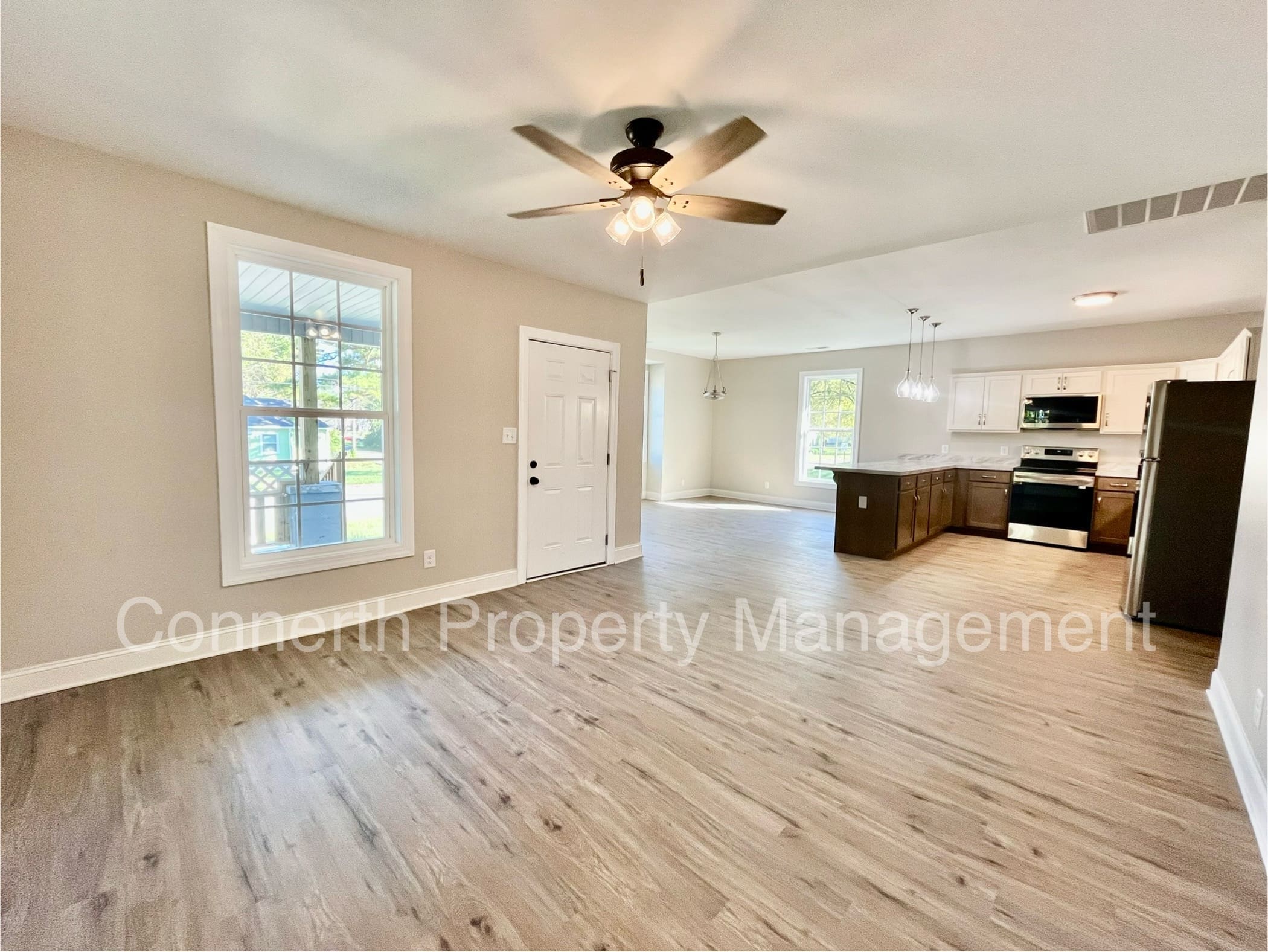 Spacious open-concept kitchen and living area with light wood flooring, ceiling fan, large windows, and modern appliances.