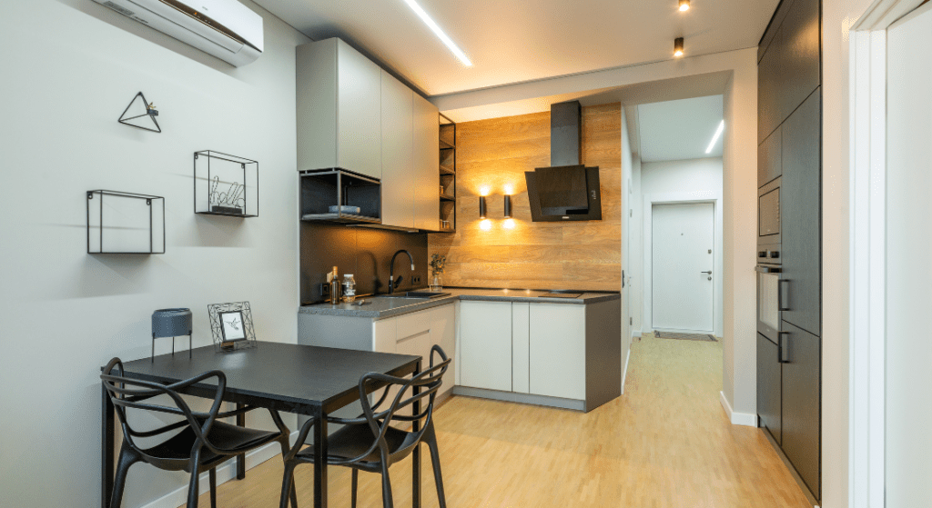 Modern kitchen with light wood flooring, white and black cabinets, wall-mounted shelves, and a dining table with four chairs. Renting in Woodridge Estates, Clarksville TN