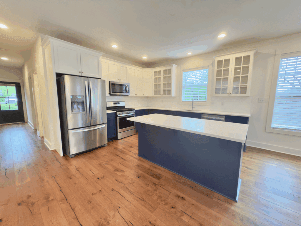Modern kitchen with stainless steel appliances, white cabinets, blue island, wood flooring, and large windows with blinds.