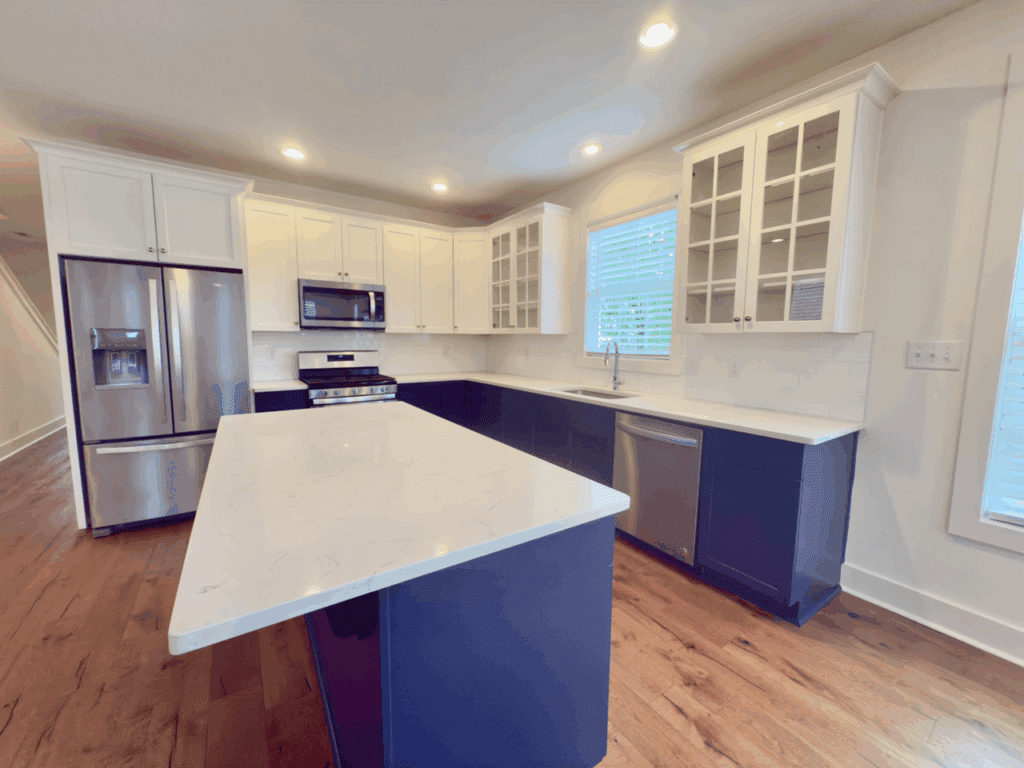 Modern kitchen with white upper cabinets, navy blue lower cabinets, stainless steel appliances, center island, and wood flooring.