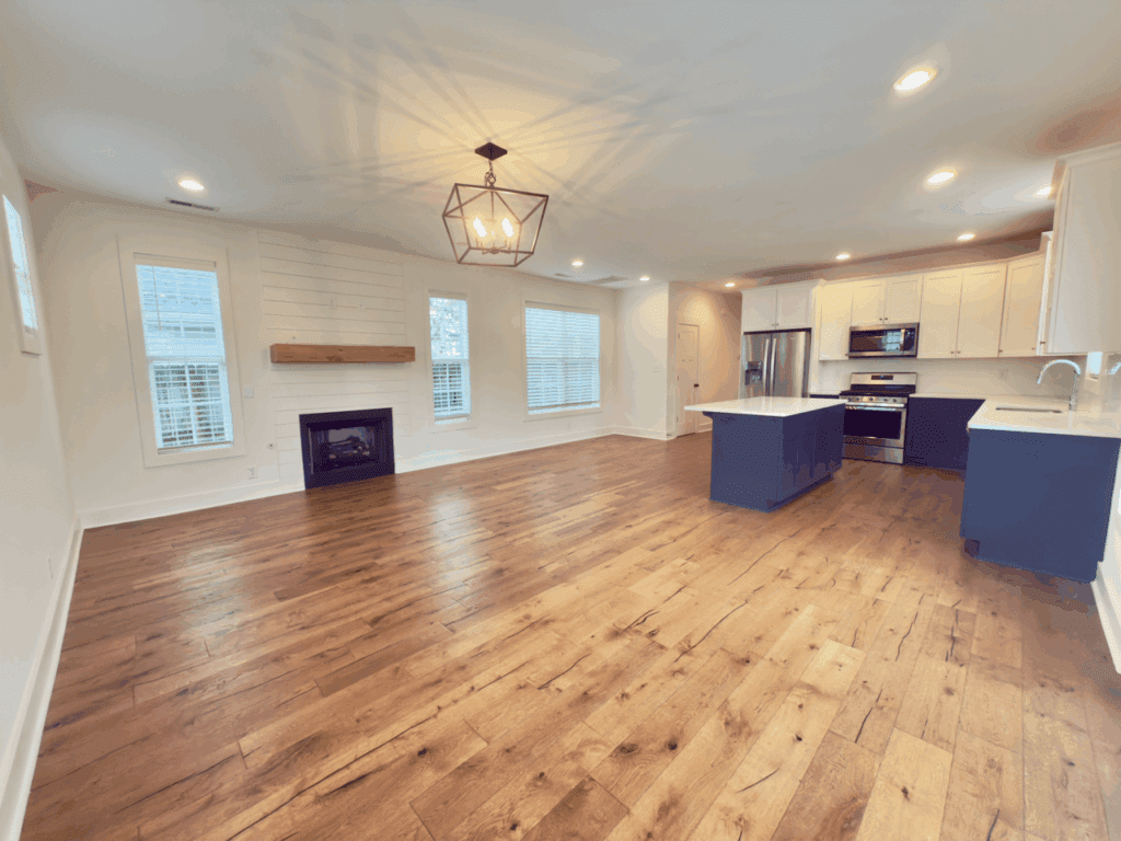 A spacious open-concept living area with wood floors, a fireplace, large windows, and a modern kitchen featuring white cabinets and a blue island.