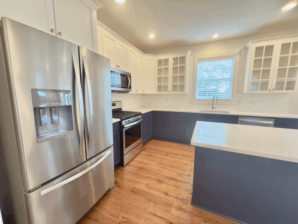 Modern kitchen with stainless steel appliances, white upper cabinets, dark lower cabinets, glass cabinet doors, a large sink, and wood flooring.