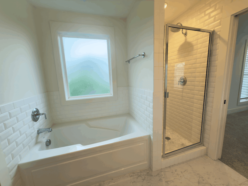 A bathroom with a white bathtub beneath a frosted window, next to a glass-enclosed shower with tiled walls and chrome fixtures.
