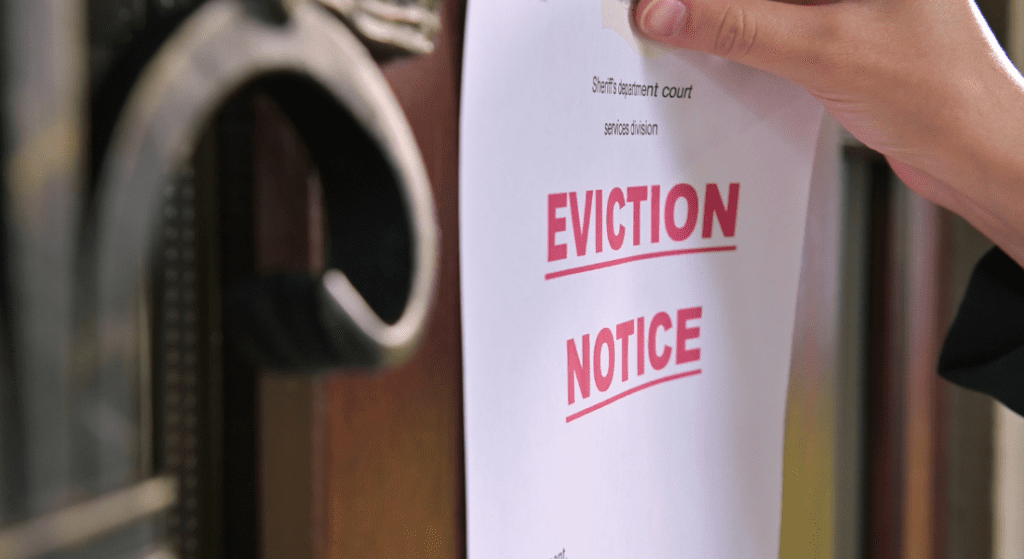 A person posts a paper labeled "Eviction Notice" on a door, using tape.