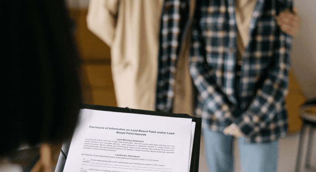 A close-up of a clipboard holding a lead-based paint disclosure form with two people standing together in the background.