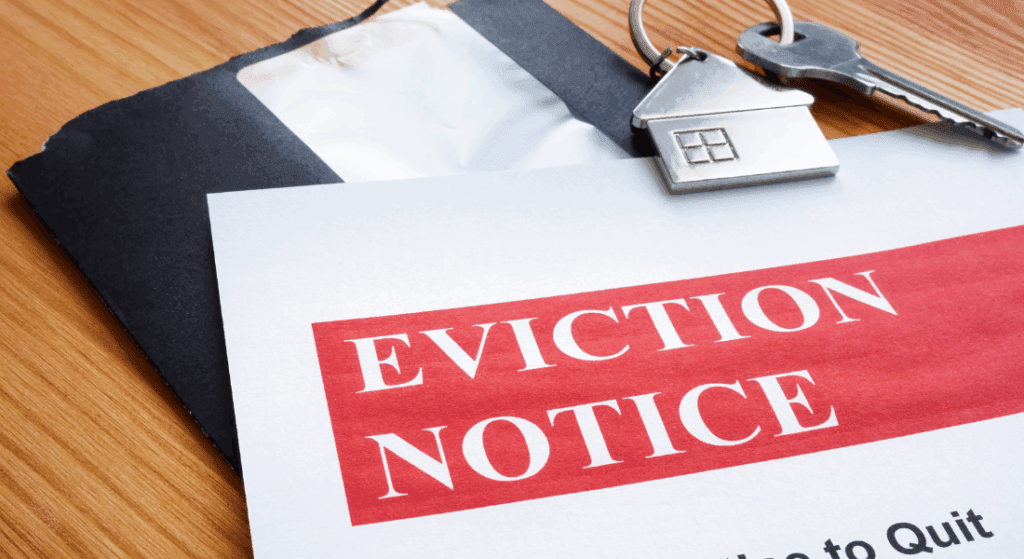 An eviction notice document on a wooden table, next to a black envelope and a key with a house-shaped keychain.