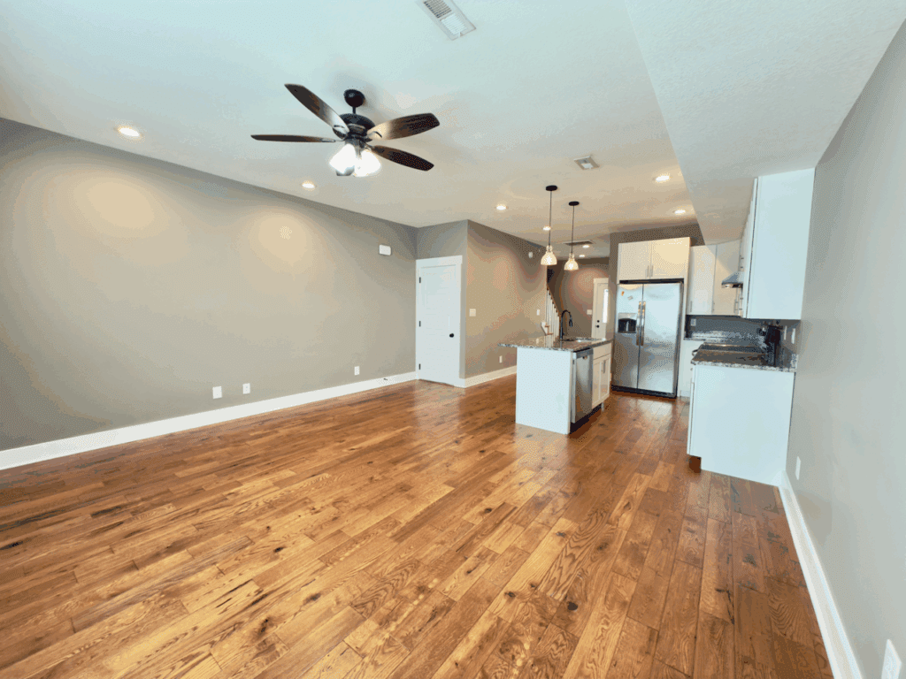 Open-plan living area with hardwood floors, ceiling fan, recessed lighting, and a kitchen featuring white cabinets, stainless steel appliances, and an island with pendant lights.