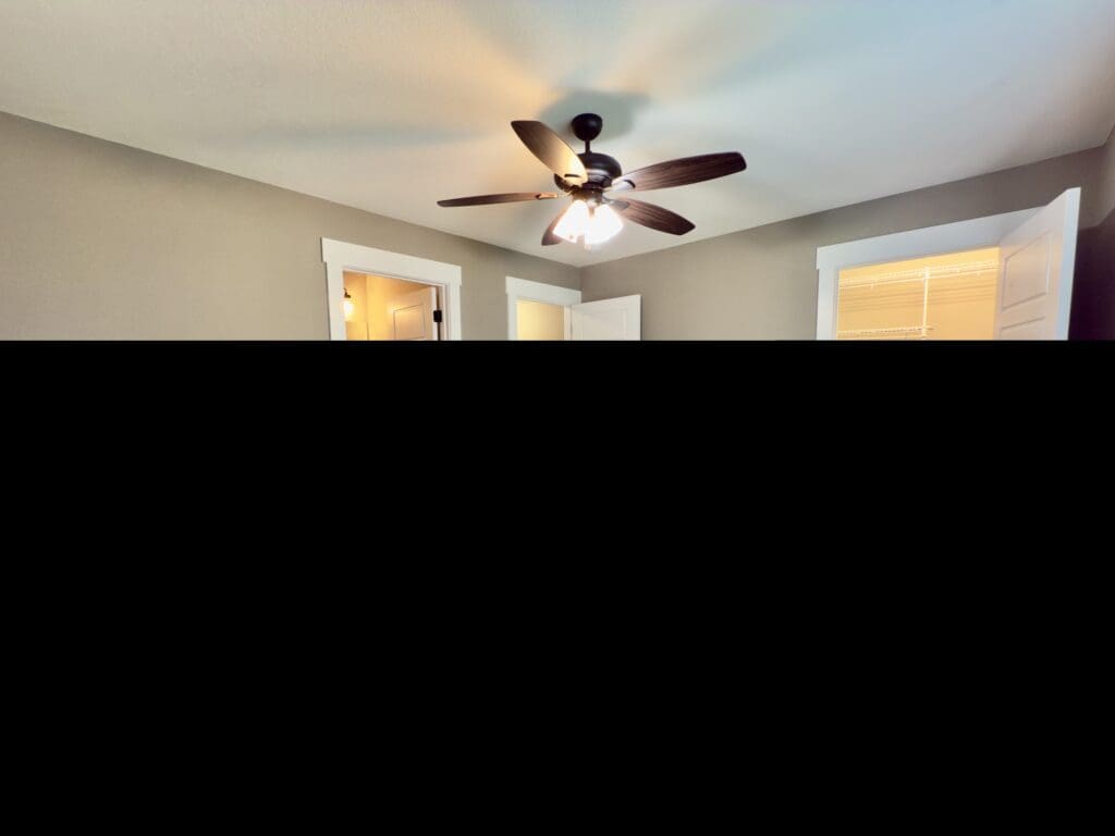Empty bedroom with carpeted flooring, a ceiling fan with lights, and three white doors leading to a bathroom, closet, and hallway.